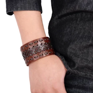 Braunes gothic geflochtenes Leder-Cuff-Armband getragen am Handgelenk mit Denim-Hintergrund, zeigt die charakteristische Kreuzbindungs-Textur und den versteckten Druckknopf-Verschluss