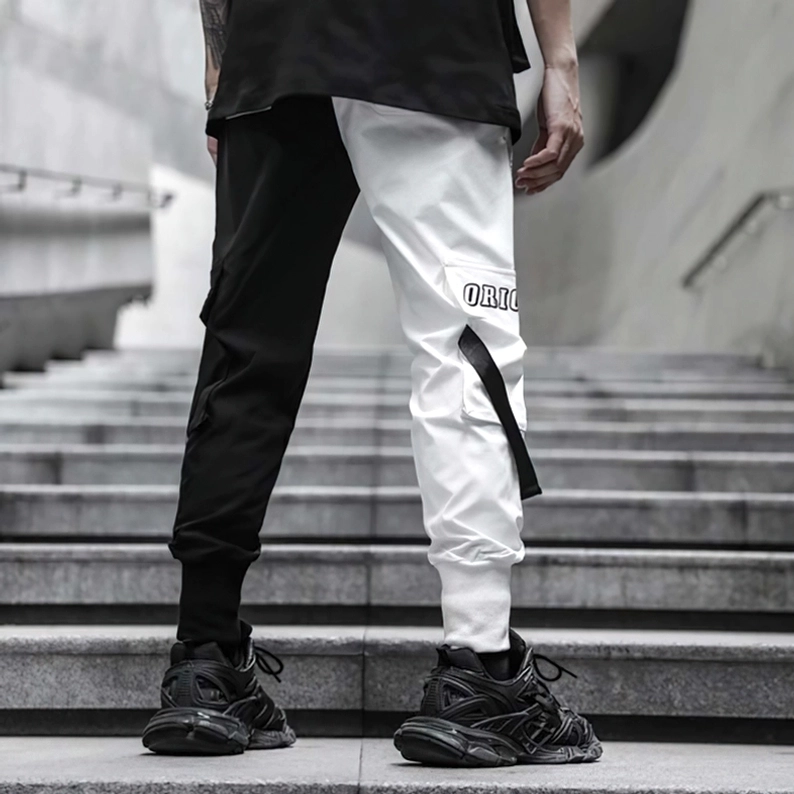 Rückaufnahme der schwarzen und weißen Gothic-Patchwork-Cargo-Hose mit Text-Patch-Labels, Utility-Details und gerippten Knöchelbündchen im Freien