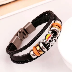 Mehrschichtiges Gothic Schädel Armband mit farbigem emailliertem Schädelanhänger und warmen metallischen Abstandsperlen auf geflochtenem Leder – Draufsicht Tischaufnahme des Charm-Details
