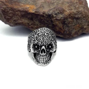 Dunkler silberner gotischer Totenkopfring auf rustikalem Steinuntergrund, detaillierte geschnitzte Blumenmuster auf dem gesamten Schädel, Punk-Rock-Alternative Schmuckstücke mit antiker Patina