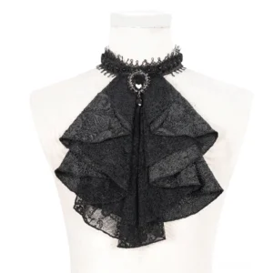 Schwarze Jabot-Halsbinde mit gefältelten Lagen und ornate Edelstein-Brosche auf weißer Schneiderpuppe, Frontalansicht Detail