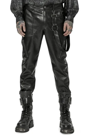Schwarze Gothic PU-Lederhose Vorderansicht auf tätowiertem männlichem Model – taillierte Silhouette mit abnehmbarem schwarzem Harness-Riemen und D-Ring Hardware, kombiniert mit schwarzem Gothic-Langarmshirt und Plateau-Stiefeln
