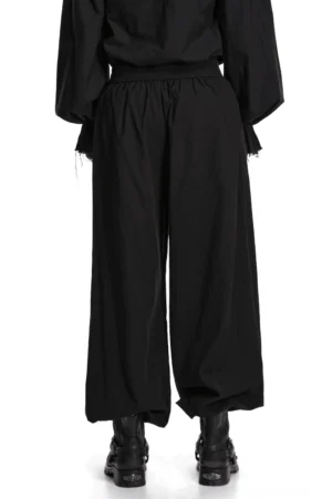 Schwarze gotische Schlaghose Rückansicht auf Model, elastische Taille und eleganter Stoff-Fall mit gerafften Knöchel-Bündchen