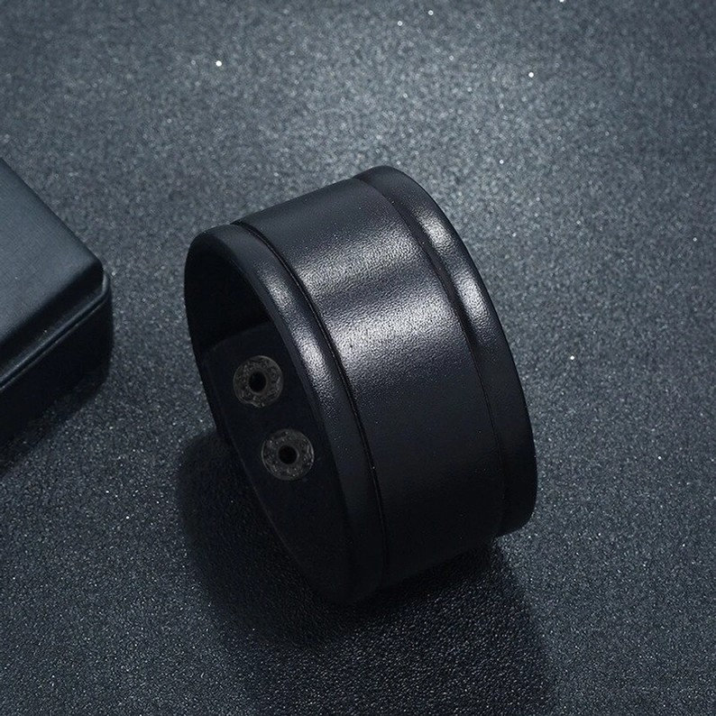 Schwarzes breites Leder-Gothic-Armband in seitlicher Flachlage, zeigt inneren Snap-Button-Verschlussmechanismus und die handgefertigten Lederkanten