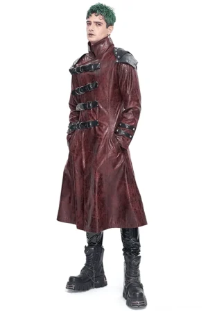 Weinrote studded gothic trenchcoat mit multi-buckle harness system front three-quarter ansicht auf männlichem model mit grünem haar und schwarzen combat-boots